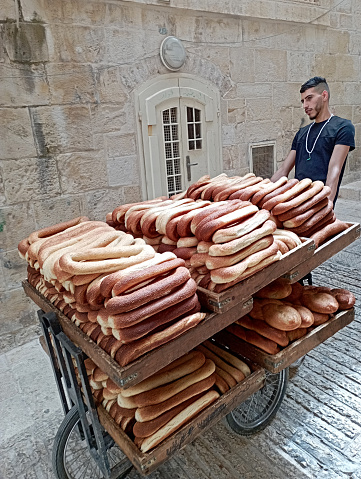 In the Old City of Jerusalem, a young baker is pulling a cart fully  loaded with fresh arab bagels .
Jerusalem bagel, called 