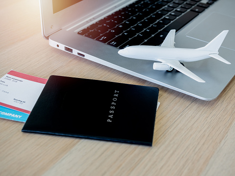 white airplane toy on the laptop computer with passport black cover and flight ticket on wooden desk. Online ticket booking for travel concept.