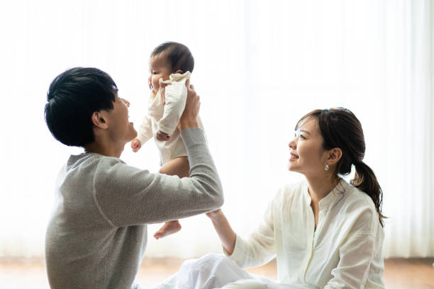 eine mutter und ein vater, die ihr baby hochhalten - baby newborn chinese ethnicity asian ethnicity stock-fotos und bilder