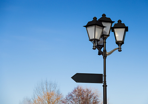 street large, black lantern with three lamps against the blue sky. Close-up, copy paste. Arrow pointer. Cityscape, summer day