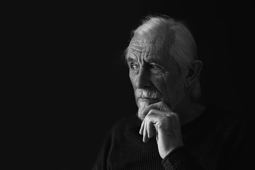 Low key black and white portrait of pensive gray hair old man looking at free place for your text. Horizontally.