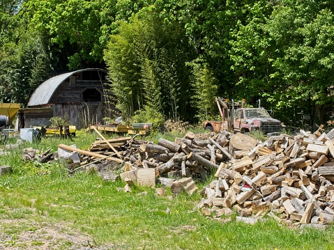 Rural homestead in decay outside Maggie Valley North Carolina in May 2022. Wood piles serve as primary heating in the Appalachian homestead. An old wrecker is in the background as well as a decaying barn and other personal belongings.