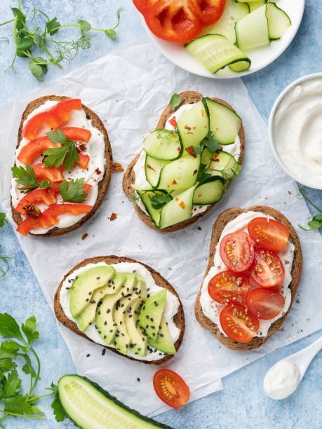 Open sandwiches (bruschetta) with ricotta cheese, cherry tomatoes, avocado slices and cucumbers. Top view. Healthy breakfast or lunch concept. Vegetarian food or snack. Toasted bread with vegetables and dry herbs. cream cheese photos stock pictures, royalty-free photos & images