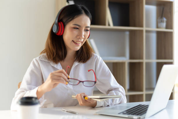 istock Woman holding a notepad and eyeglasses watching a laptop screen. Online learning style from home. 1398651271