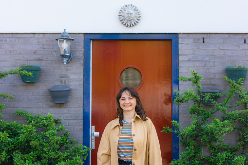 Young Caucasian woman standing and smiling on the background of front door