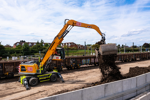 Peterborough, UK - May 17, 2022.  A heavy plant digger machine unloading spoil and earth from the wagons of a freight train after railroad engineering works during the UK HS2 rail project