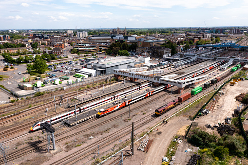 Peterborough, UK - May 17, 2022.  An aerial landscape view of passenger and freight trains waiting on the platforms of Peterborough train station on the East Coast Main Line railway with the city in the background