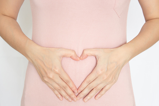 Woman are make heart hand gesture in front of her tummy to express pregnant or good health of digestion and diet.