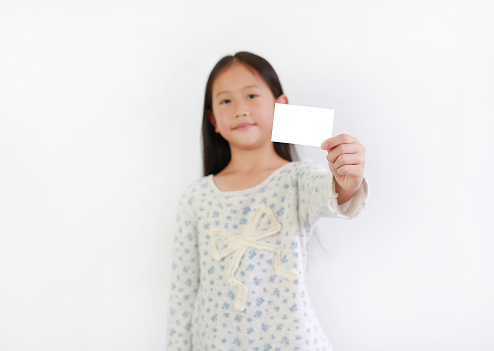 Asian girl kid showing blank white card over white background. Focus at card in child hand.