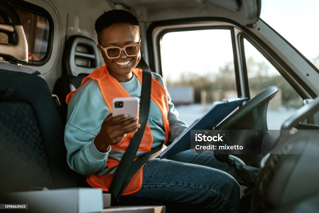 Young smiling female delivery driver texting while working Young smiling female delivery driver texting while working, she is inside of a delivery van Delivery Person Stock Photo
