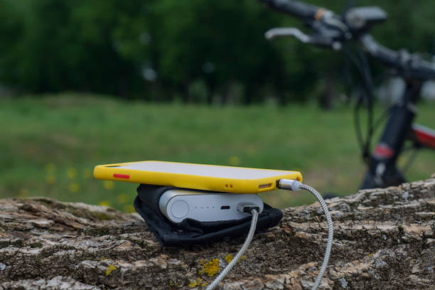 A portable charger charges the smartphone. Power Bank with cable against the background of wood and bicycle A portable charger charges the smartphone. Power Bank with cable against the background of wood and bicycle. bicycle docking station stock pictures, royalty-free photos & images