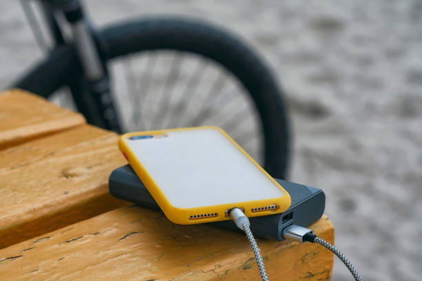 A portable charger charges the smartphone. Power Bank with cable against the background of wooden bench and bicycle. A portable charger charges the smartphone. Power Bank with cable against the background of wooden bench and bicycle bicycle docking station stock pictures, royalty-free photos & images