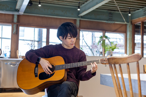 A man in his twenties practicing playing the guitar\nPerforming arts repeatedly practice
