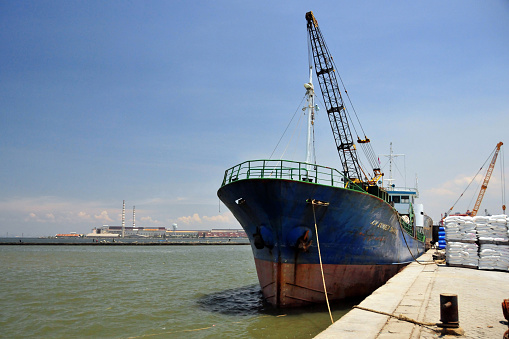 Jakarta, Java, Indonesia: freighter ship at Sunda Kelapa harbor with cargo on pallets on the pier, KM Sumber Kahaya - old port on the Ciliwung River estuary - power-station in the background (Muara Karang Combined Cycle Power Plant).