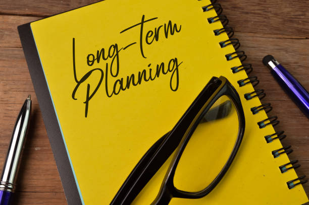 Top view of pen, eyeglasses and notebook written with LONG-TERM PLANNING