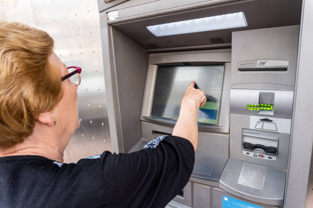 istock Elderly woman using an ATM in the street 1398671342