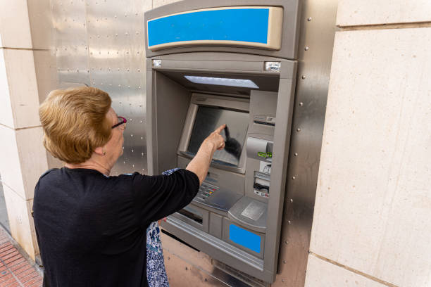 istock Elderly woman using an ATM in the street 1398671685