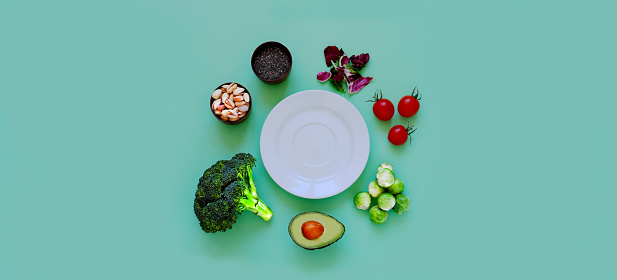 Ingredients for proper nutrition and empty white plate on green background. The concept of healthy diet or summer background. Close-up, copy space