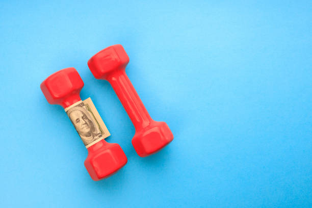 istock two red dumbbells and one hundred dollars on a blue background 1398673100