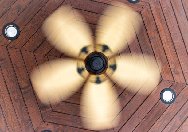 A ceiling fan spins around under the wooden ceiling of an outdoor porch.