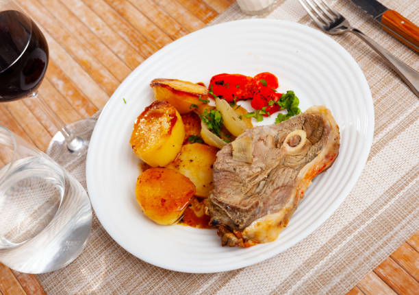 Portion of roasted lamb leg with potatoes and pepper served on plate.