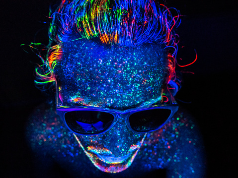 Long hair man under a UV light, wearing eyeglasses and looking down