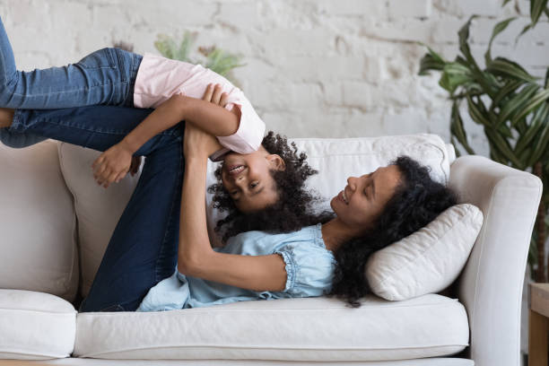 Cheerful Black mom and daughter kid playing active games Cheerful Black mom and preschool daughter kid playing active games on sofa, having fun at home. Mum cuddling, tickling child, lifting girl in air, doing acroyoga, laughing, enjoying family leisure acroyoga stock pictures, royalty-free photos & images