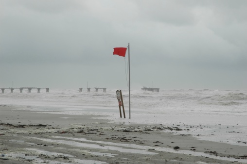 Hurricane on the coast of Alabama.  Waves crashing against damaged pier.  Red warning flag flying in the foreground.