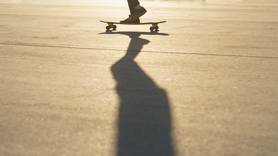 Leisure activity in summer day. Sportive lifestyle. Young man riding skateboard. Photography of feet and skateboard. Close up photography. Low angle view. Back lit image