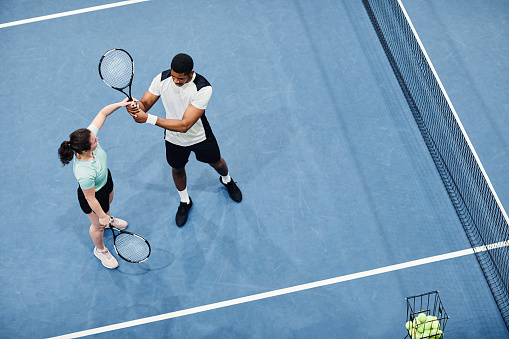 Minimal top view of tennis coach working with client against vibrant blue court, copy space