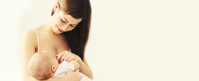 Portrait of happy young mother feeding breast her baby on white background, blank copy space for advertising text