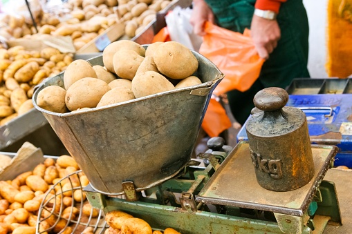 5 kilogram of fresh potatoes on an old fashioned libra with a weight, at a farmers market. Potato farmer in background. This image is part of a series.