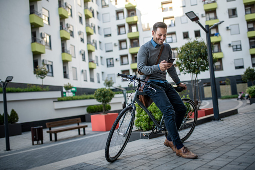 A casual businessman sits on a bike a using smartphone