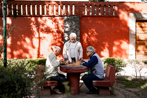 Three senior friends spending time outdoors playing chess