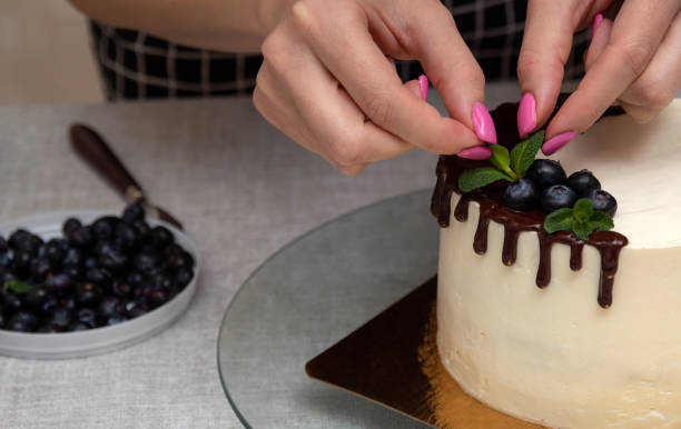istock Women's hands add a mint leaf to the cake decoration, next to blueberries in chocolate. Image for a website about food, confectionery. Selective focus. 1398705476