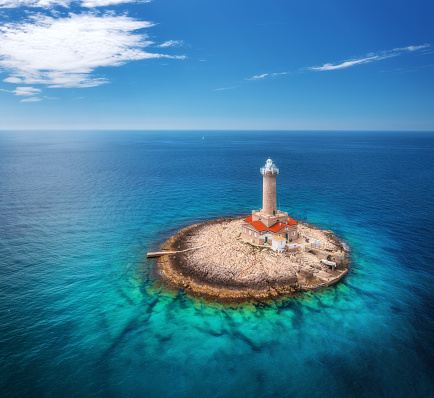 Lighthouse on smal island in the sea at sunny day in summer. Aerial top view of beautiful lighthouse on the rock, clear azure water and blue sky with clouds. Landscape. Adriatic sea, Croatia. Travel