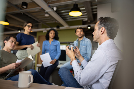 Latin American business man showing a 3D printing model to his team in a meeting at the office - innovation concepts