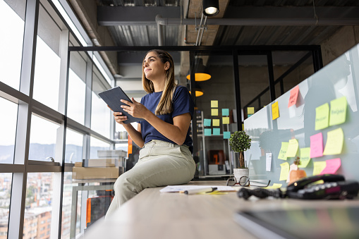 Thoughtful woman working at the office and thinking of ideas while holding a tablet computer