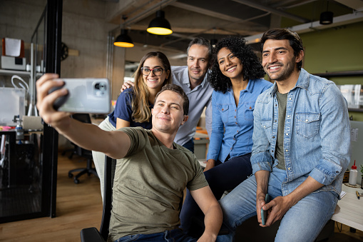 Happy group of creative Latin American workers taking a selfie at the office using a cell phone - teamwork concepts