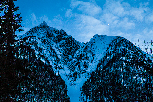 Night winter scene of snow capped rocky mountains with clear sky and crescent moon