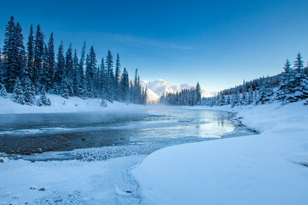 idyllic winter scene of bright blue snowmelt river, snow covered mountain landscape and bright blue sky - spring forest scenics reflection imagens e fotografias de stock