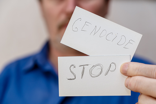 Stop War. The writing is in jagged gray letters on the paper. Man holds two white paper rectangles with handwritten text in front of his face. Close-up of a mature man's hand.