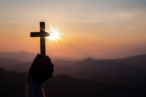 Human hand holding cross with light sunset background. christian concept