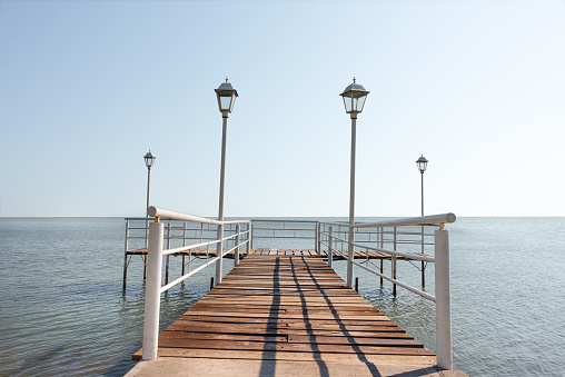 Wooden and metal pier with lampposts during a cloudless summer day with a calm sea without boats, no people