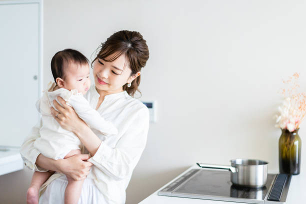 赤ちゃんを抱きながら家事をしている若い女性 - breastfeeding mother newborn baby ストックフォトと画像