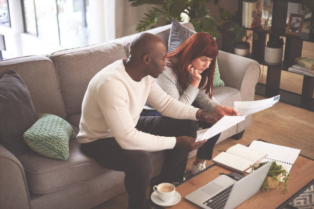istock A couple going through paperwork at home and using a laptop. A young man and woman paying bills, planning their finance and looking at paper online with a computer on the sofa 1398738099