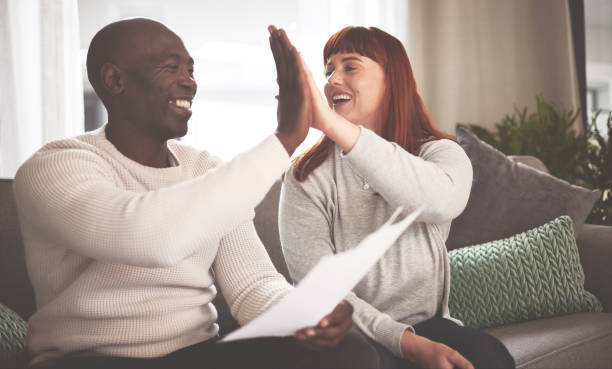istock A couple celebrating and giving a high five while going through paperwork at home. A happy young man and woman paying bills, planning their finance and looking at paper on the sofa 1398738196