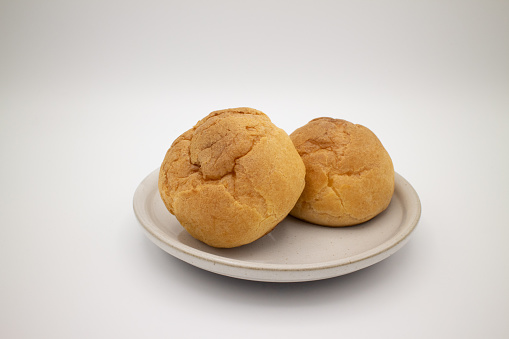 Two delicious cream puffs are on a white ceramic plate, with white background.