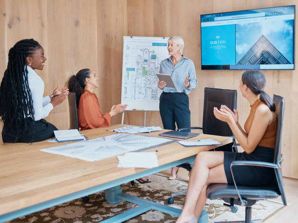 istock Mature caucasian businesswoman smiling and standing using a tablet while giving a presentation in the boardroom during a meeting with her female only diverse multiracial colleagues in a workplace 1398740209