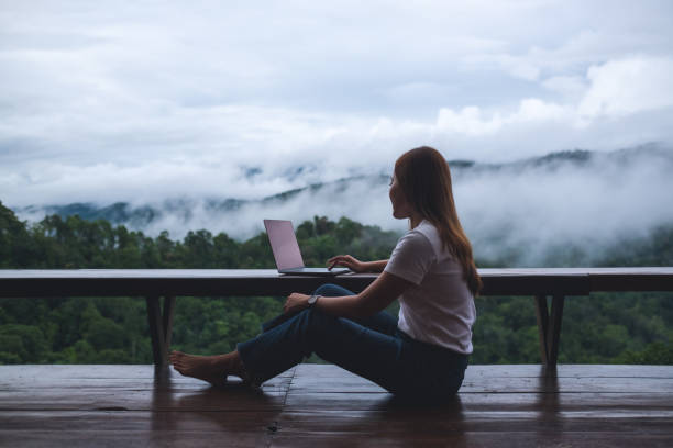 istock A young woman using and working on laptop computer while sitting on balcony with a beautiful nature view on foggy day 1398740236